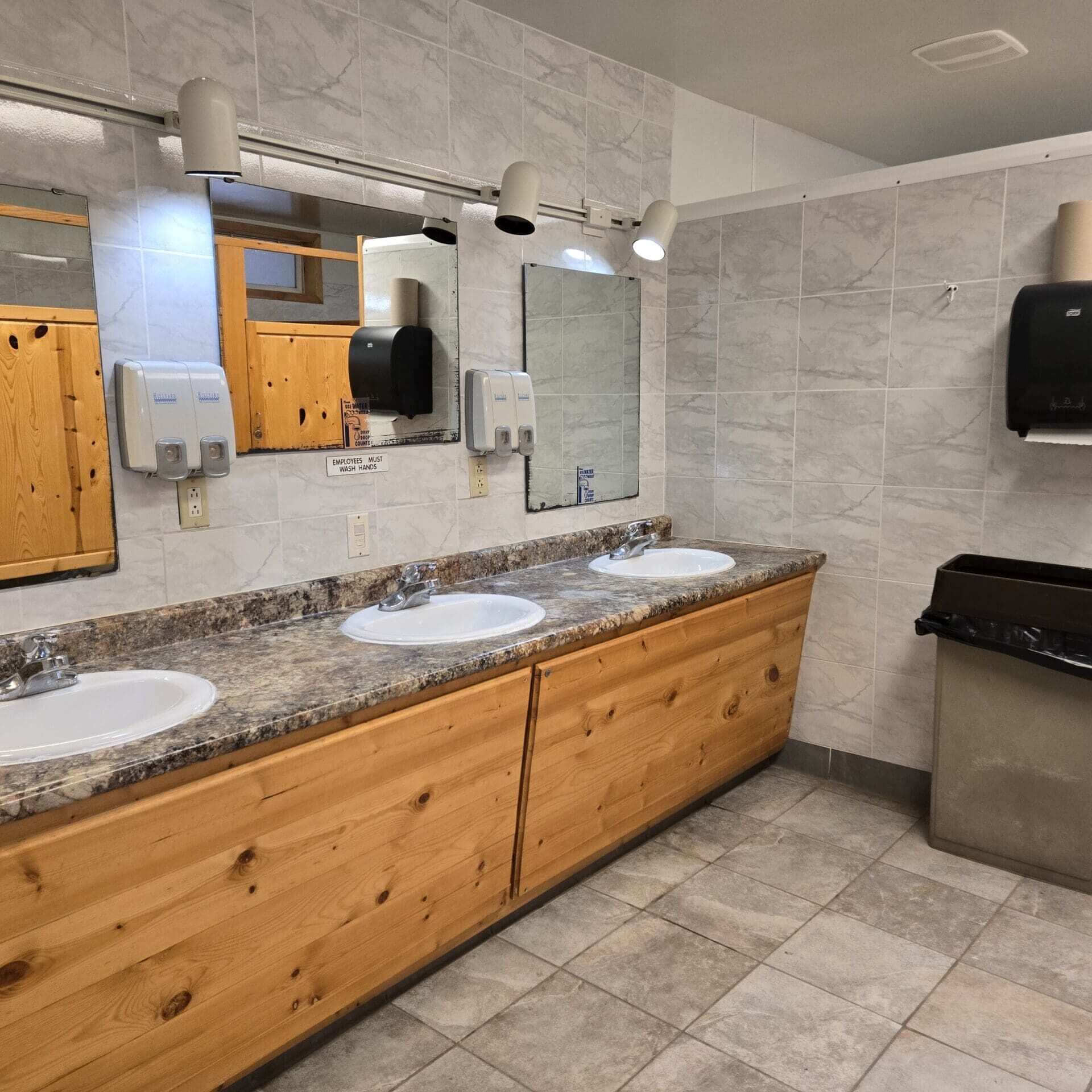 Bathhouse interior vanity with multiple sinks, mirros and paper towel dispenser and trash can at Beaver Lake Campground